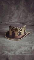Vintage Brown Top Hat with Art Deco Inspired Gold Patterns and Ribbon on Fabric Background photo