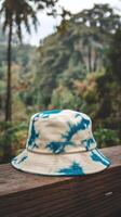 Blue And White Tie Dye Bucket Hat On Wooden Railing With Tropical Forest Background Outdoors photo