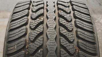 Closeup of black car tire tread with intricate geometric patterns on concrete surface background photo