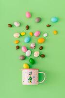 Spring composition made with colorful chocolate Easter eggs and pink mug on pastel green background. Minimal Easter concept. Creative festive holiday layout. Easter aesthetic. Flat lay, top of view. photo