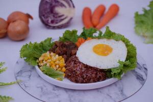 A vibrant meal consisting of red rice, meat, corn, carrots, lettuce, and a sunny side up egg photo