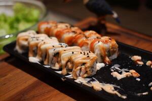 Sushi roll with salmon, avocado, cheese and sauce on black plate photo