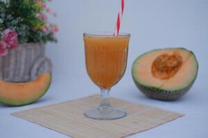 A glass of melon juice accompanied by fresh melon slices on the table. photo