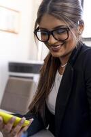 smiling portrait of beautiful business woman with eyeglasses using yellow mobile phone inside modern office photo