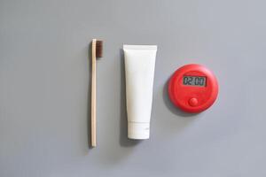 Eco friendly bamboo toothbrush with toothpaste tube and red digital timer on gray background. photo