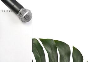 Microphone above white notebook with green leaves on black background for creative writing and expression. photo