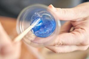 Close up of hands mixing blue epoxy resin in clear plastic cup with wooden stick. photo