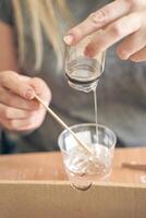 Young caucasian female mixing resin in a cup using a wooden stick for craft projects. photo