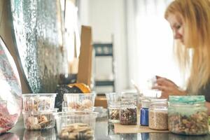 Caucasian female adult creating handmade crafts with assorted stones and containers in sunlit workspace. photo