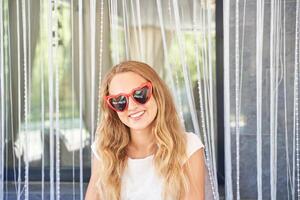Young caucasian female in heart shaped sunglasses smiling in front of curtain background. photo