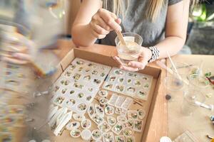 Female artisan crafting resin jewelry with decorative elements in workshop setting. photo