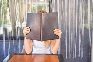 Caucasian female adult reading menu at restaurant table with beaded curtain background. photo