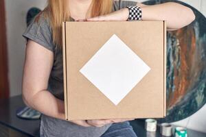 Caucasian female holding cardboard box with blank label in casual setting. photo