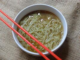 instant noodle soup in a white ceramic bowl. red chopsticks. photo