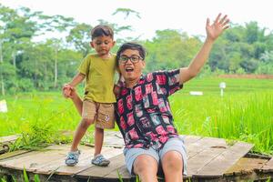 pequeño chico participación manos con padre mientras en arroz campo foto