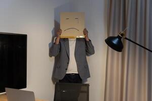 Portrait of a businessman covering his face with a paper mask with a sad face, drawn on it Bad negative depression. photo