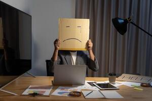 Portrait of businessman covering his face with paper mask with sad face drawn on it, bad negative. photo