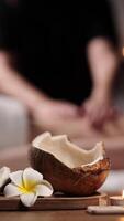 Close-up Tropical coconut, candle, Frangipani flower against blurred spa background. Female relaxing massage with Coconut oil. Selective focus. Luxury, tranquility in beauty salon. Vertical shot, ads video