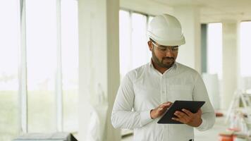 Indian construction engineer reviewing building project with tablet on-site video