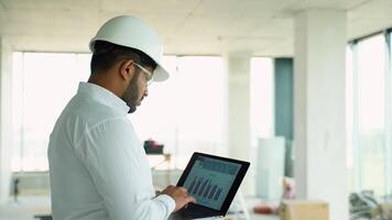 Indian engineer reviewing construction project data with a laptop on-site video