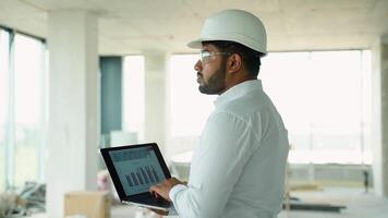 Indian engineer analyzing construction project data on-site using laptop video