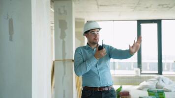 A male engineer using a walkie-talkie and giving directions to workers at a construction site video