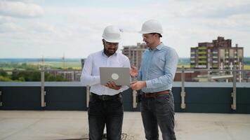 Two construction engineers discussing project data on rooftop site video