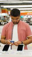 Indian man choosing a new smartphone in a tech store. Vertical video