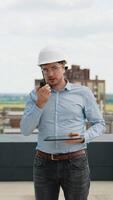 A builder engineer on a construction site uses a walkie-talkie and a tablet for project coordination video