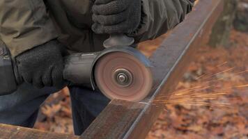 A worker in gloves operates a power grinder on metal, producing bright sparks in a forested area during daylight, focused on a precise cutting task. video
