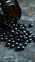 Black dietary supplements scattered from glass bottle on marble surface photo
