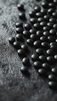 Detailed close-up view of black round pills scattered on a textured surface photo