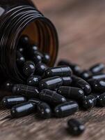 Black capsules spilled from an open bottle on a wooden surface photo