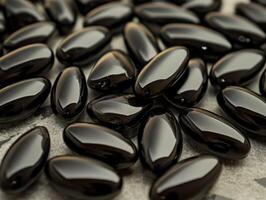 Black glossy capsules scattered on a textured surface in natural light photo