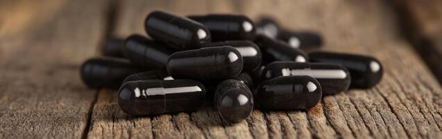Black herbal capsules scattered on a rustic wooden surface photo