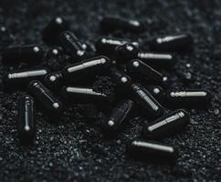 Black capsules scattered on a dark textured surface during evening light photo