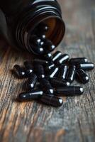 Black capsules spill from a glass bottle onto a wooden surface photo
