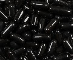 Black capsules arranged closely on a surface ready for consumption photo