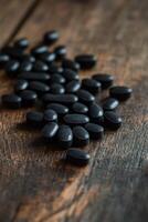 Black oval pills scattered on a rustic wooden surface during daylight photo