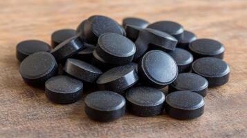Black circular tablets arranged on a wooden surface in a natural setting photo
