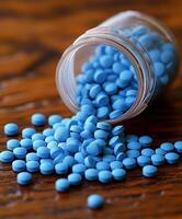 Blue tablets spill from a glass container onto a wooden surface photo