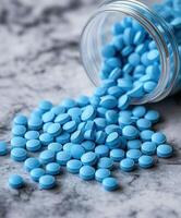 Blue tablets scattered from a glass jar on a textured surface photo