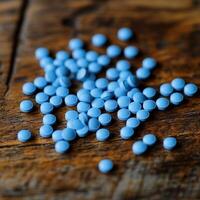 Blue pills scattered on wooden surface, natural light highlighting texture photo