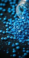 Blue pills scattered on dark surface near an overturned jar photo