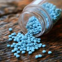 Blue pills scattered from a glass jar on a rustic wooden surface photo