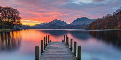 Sunset over tranquil lake with pier and mountains in the background photo