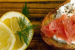 Delicious open-faced sandwich with smoked salmon and lemon slice on wooden board photo