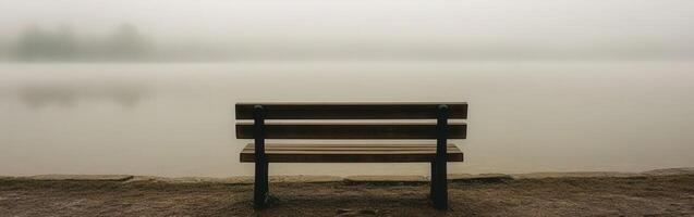 Lonely bench by the tranquil lake surrounded by early morning fog photo