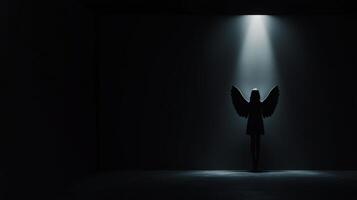 Silhouette of a figure with wings illuminated in a dark space photo