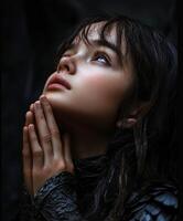 Young woman with hands clasped in prayer under dark lighting photo
